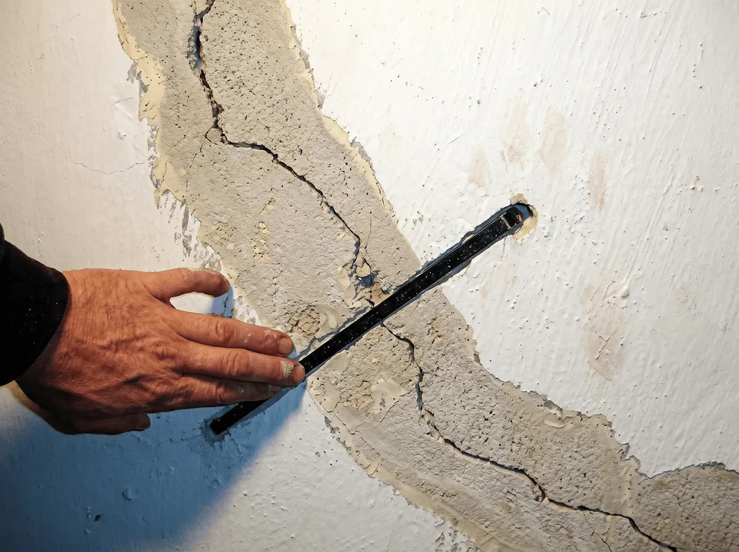 A wall with a large crack is being inspected by a professional in Newark, NJ